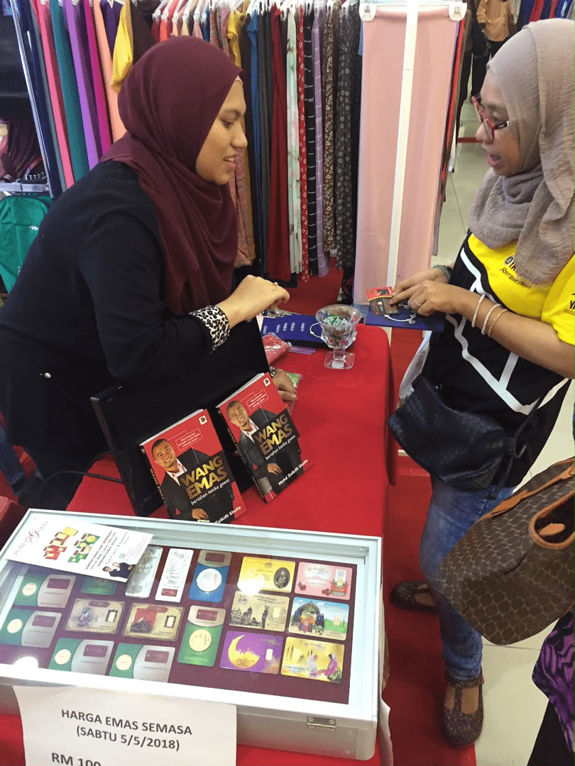 Puan Syamimi mengendalikan kaunter booth bersama naskhah buku Wang Emas Tuan Zul dan kotak pameran emas Public Gold pada Mei 2018