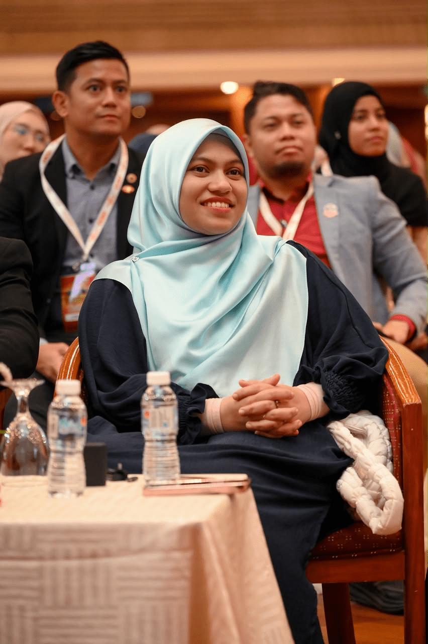 Potret Puan Syamimi Nur Aqila berhijab biru duduk di barisan hadapan pemimpin utama semasa persidangan konvensyen